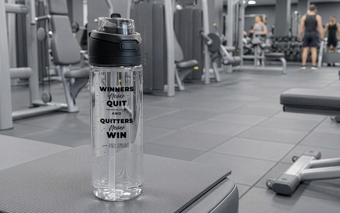 Transparent RETUMBLER-URBIX sports bottle with motivational quote standing on a bench in the gym