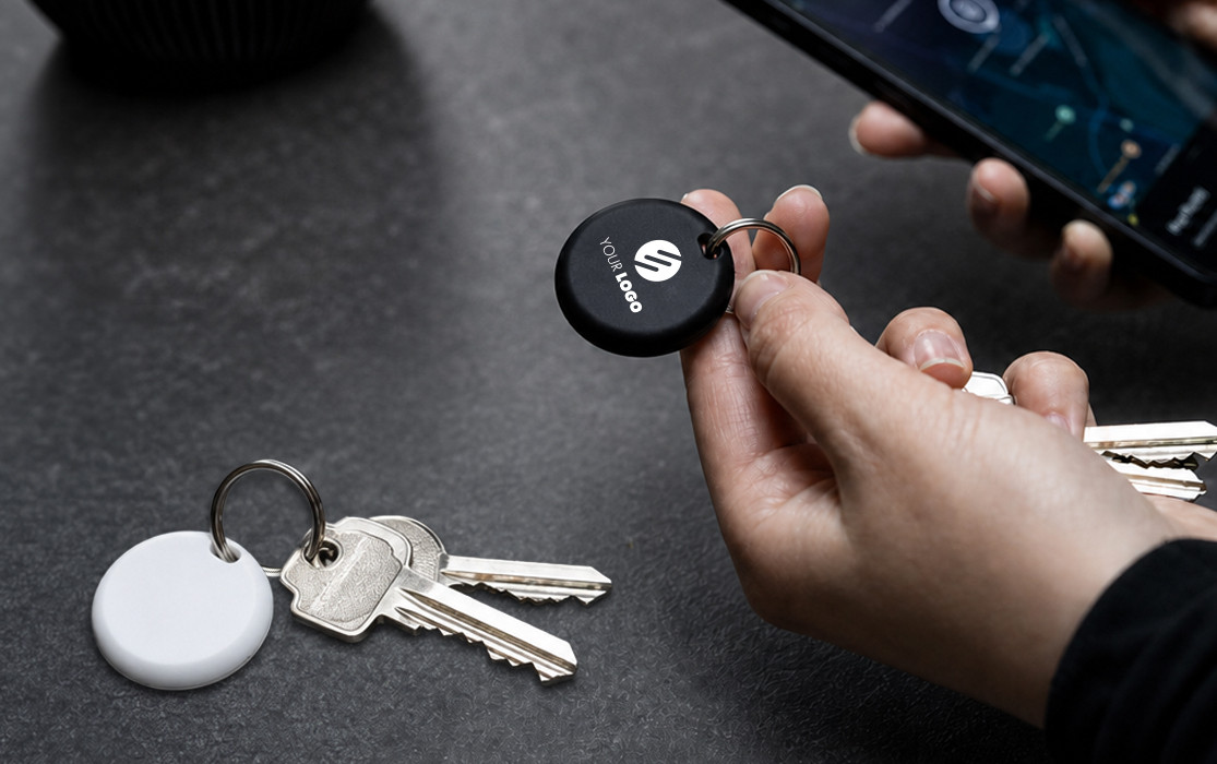 Locator tag for keys Black locator tag for finding keys on a key ring, held in hand next to keys and smartphone.