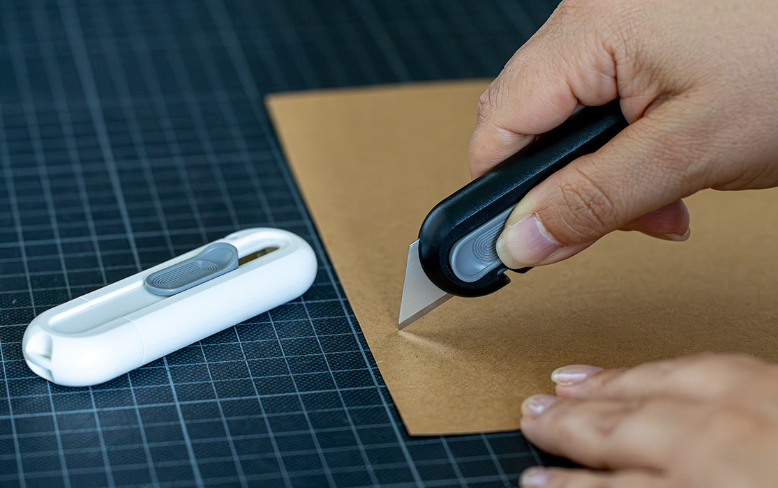 Hand mit Cutter in einer Testsituation neben einem weißen technischen Gerät auf einer Schneidematte.