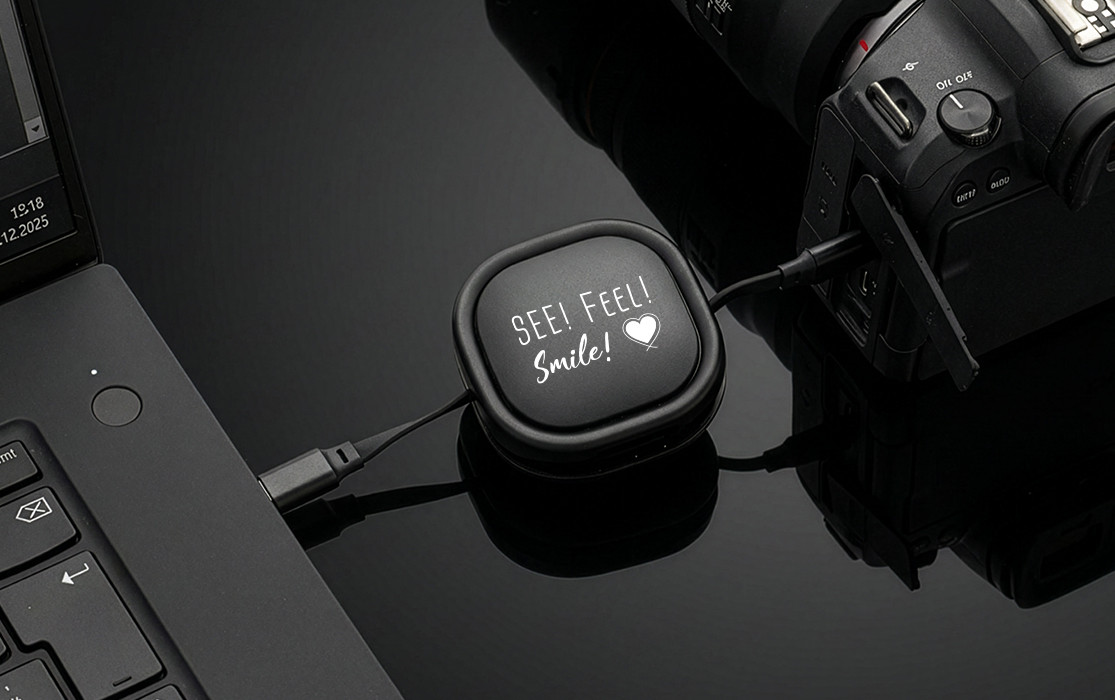 REEVES-KALVERO data and charging cable, connected to a laptop and a camera, with “SEE! FEEL! Smile!” engraving on a black background