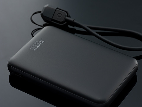 Black power bank for mobile charging with connected charging cable on a dark background.