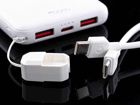White power bank for mobile charging with USB ports, charging cable and adapter shown in close-up.